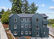 Thumbnail 40 of 50 - A large grey building with a black roof and multiple windows.