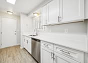 Thumbnail 24 of 40 - A white kitchen with wood floors and stainless steel appliances.