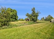 Thumbnail 9 of 40 - A lush green field with trees and a house in the distance.