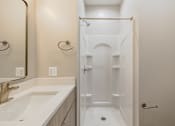 Thumbnail 6 of 14 - A white bathroom with a sink, mirror, and shower.