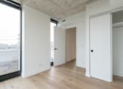 Thumbnail 18 of 81 - A room with white walls and wooden floors, with a door on the right side.