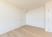 Thumbnail 53 of 81 - A room with white walls and wooden flooring with two doors.