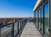 Thumbnail 40 of 81 - A balcony with glass railings overlooks a cityscape.
