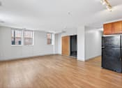 Thumbnail 12 of 20 - A black fridge sits in a room with wooden floors and white walls.