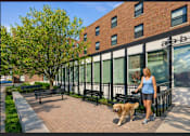Thumbnail 1 of 20 - A woman walking her dog in front of a brick building.