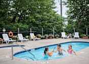 Thumbnail 12 of 58 - Three children playing in a pool surrounded by lounge chairs and greenery.