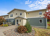Thumbnail 8 of 9 - A house with a grey and beige exterior and a small garden in front.