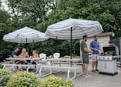 Thumbnail 18 of 58 - A group of people are gathered around a table under a striped umbrella.