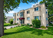 Thumbnail 33 of 39 - A large beige building with a red awning is surrounded by a green lawn.