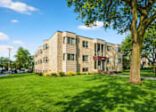 Thumbnail 2 of 39 - A large tree stands in front of a tan building with a red awning.