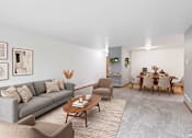 Thumbnail 49 of 58 - A living room with a grey couch, a wooden coffee table, and a dining table set up.