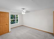 Thumbnail 37 of 59 - A room with a carpeted floor, a ceiling fan, and a window with a view of trees outside.