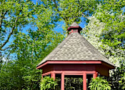 Thumbnail 57 of 59 - A red gazebo with a black roof is surrounded by trees.