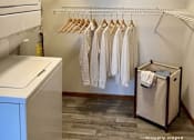 Thumbnail 25 of 59 - A laundry room with a washer and dryer, shelves with towels and other items, and clothes hanging on a rack.