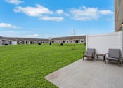 Thumbnail 3 of 23 - A row of houses with a lawn in front and two chairs on a concrete walkway.