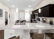 Thumbnail 8 of 18 - A kitchen with a granite countertop and brown chairs.