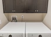 Thumbnail 17 of 18 - Two white washing machines in a laundry room with dark brown cabinets.