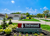 Thumbnail 3 of 18 - A sign for Redwood Apartment Neighborhoods is in the foreground of a well-kept lawn.