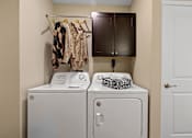 Thumbnail 18 of 18 - A laundry room with a white washer and dryer, a towel, and clothes hanging up.