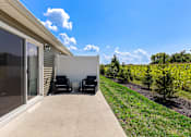 Thumbnail 6 of 18 - A patio with two chairs and a table is set up outside a house.