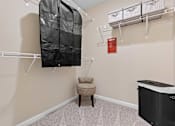 Thumbnail 10 of 20 - A baby crib sits in a room with a chair and a hanging closet.