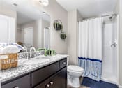 Thumbnail 20 of 21 - A bathroom with a white toilet, a sink with a marble countertop, and a shower with a white curtain.
