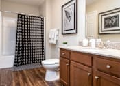 Thumbnail 14 of 19 - A bathroom with a toilet, a shower curtain, and a counter with a sink and a potted plant.