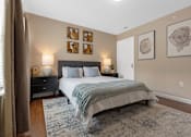 Thumbnail 9 of 19 - A bedroom with a bed, nightstand, and pictures on the wall.
