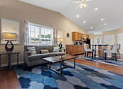Thumbnail 10 of 19 - A living room with a grey couch and a blue rug.