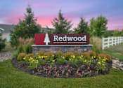 Thumbnail 19 of 19 - A sign for Redwood Apartment Neighborhoods is surrounded by flowers and greenery.