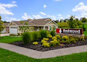 Thumbnail 4 of 19 - A well-maintained lawn surrounds a house with a sign that reads "Redwood Apartment Neighborhoods.".