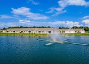 Thumbnail 10 of 19 - A fountain in the middle of a lake with houses in the background.