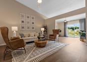 Thumbnail 6 of 19 - A living room with a grey sofa, a wooden coffee table, and a large window with a view of the outdoors.