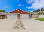Thumbnail 2 of 19 - A two-car garage with a red roof and white doors is surrounded by a gravel driveway.