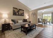 Thumbnail 7 of 20 - A living room with a beige couch, a coffee table, and a large painting on the wall.