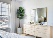 Thumbnail 18 of 25 - A bedroom with a large window, a white dresser, and a mirror.