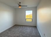 Thumbnail 6 of 18 - A room with a ceiling fan and a window showing a view of a field.