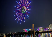 Thumbnail 11 of 12 - A firework display over a body of water with people watching.