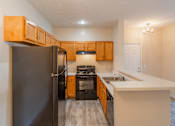 Thumbnail 9 of 19 - A kitchen with a black refrigerator and wooden cabinets.