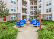 Thumbnail 32 of 63 - an outdoor patio with blue chairs and a fire pit in front of an apartment building at Vanguard Crossing, St. Louis, Missouri
