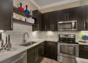 Thumbnail 19 of 52 - a kitchen with stainless steel appliances and black cabinets at Aster Apartments, Beachwood