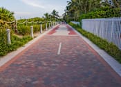 Thumbnail 6 of 12 - A red brick pathway leads through a tropical setting.