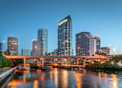 Thumbnail 8 of 12 - A cityscape at dusk with a bridge crossing a river.
