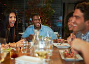 Thumbnail 9 of 12 - A group of people are sitting around a table eating and drinking.