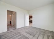 Thumbnail 16 of 36 - a living room with white walls and carpet and a door to a kitchen at Statesman Apartments, Franklin, WI