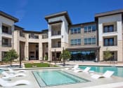 Thumbnail 9 of 40 - a pool with white chairs in front of an apartment building at Hunters Creek Apartments, Denton Texas