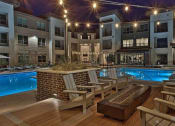 Thumbnail 13 of 40 - a swimming pool with rocking chairs in front of an apartment building at Hunters Creek Apartments, Denton Texas