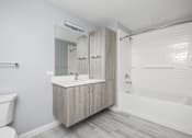 Thumbnail 39 of 69 - A white bathroom with a wooden vanity and a white bathtub.