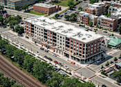 Thumbnail 30 of 66 - A large red brick building with a white roof is surrounded by other buildings and trees.