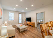 Thumbnail 6 of 9 - A living room with a white sofa, wooden coffee table, and a television.